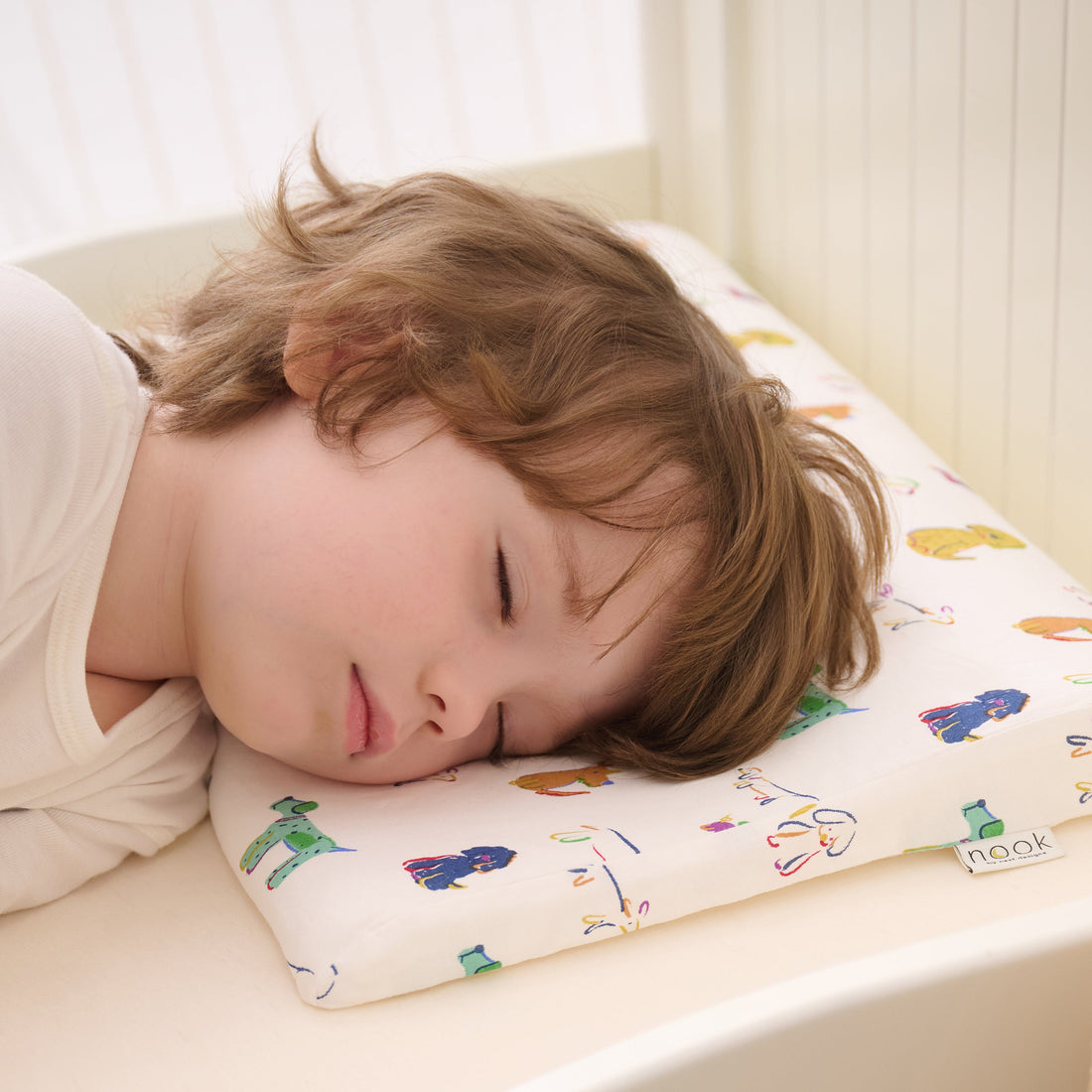 Toddler sleeping on the Bingo Nook toddler pillow in a crib