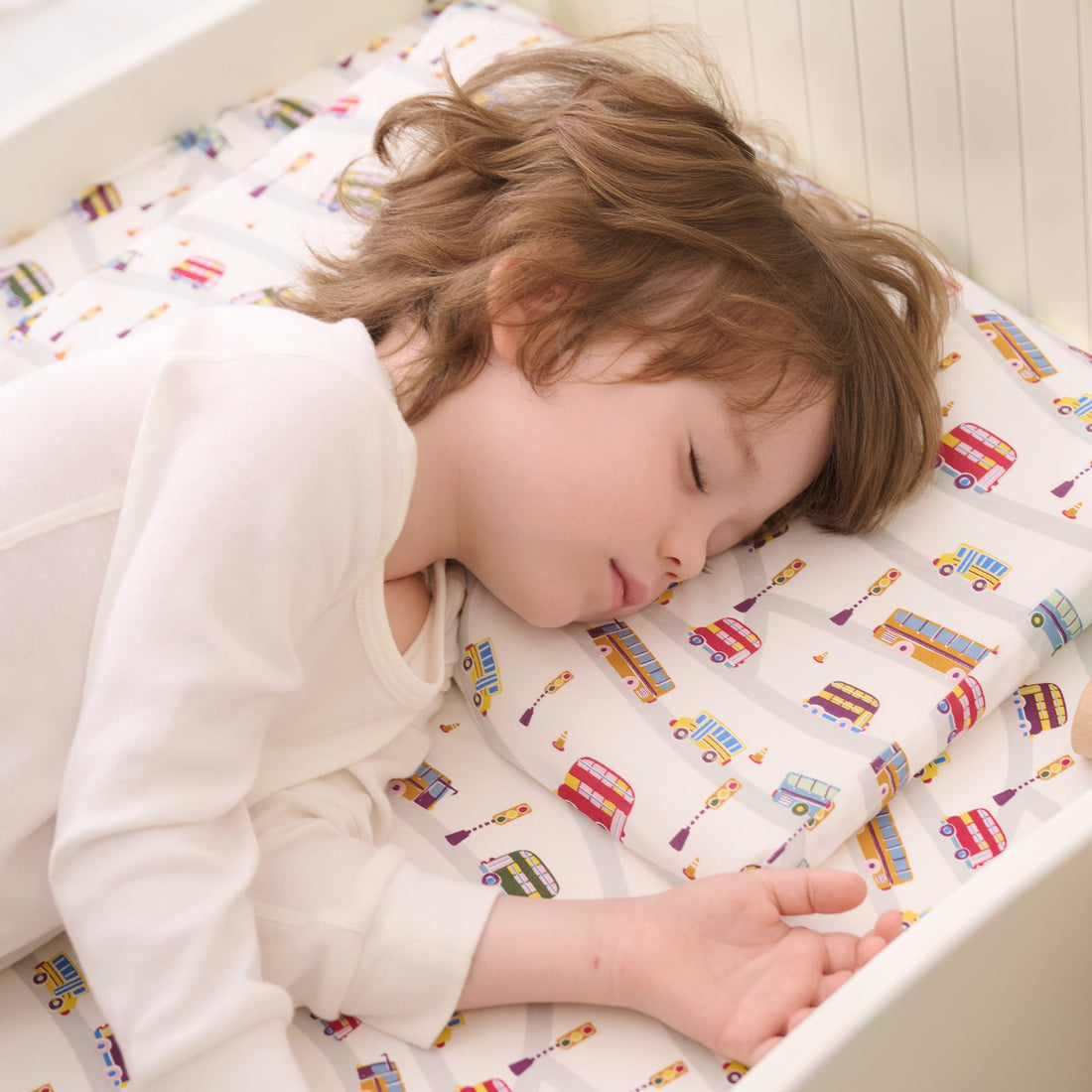 Toddler sleeping on the Wheels on the Bus Nook pillow in a crib
