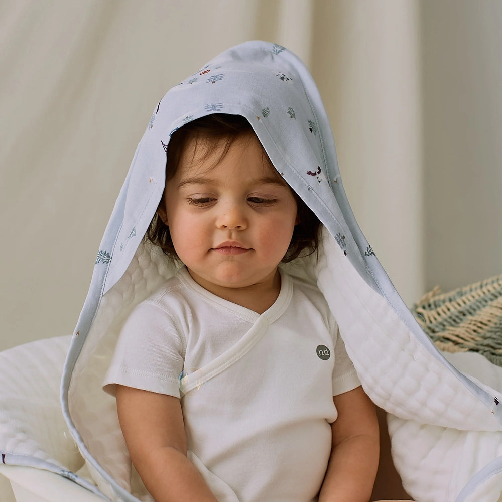 Nest Designs Organic Cotton 9-Layer Hooded Baby Bath Towel Snowy Snuggles; baby sits cozy with the hood over her head.