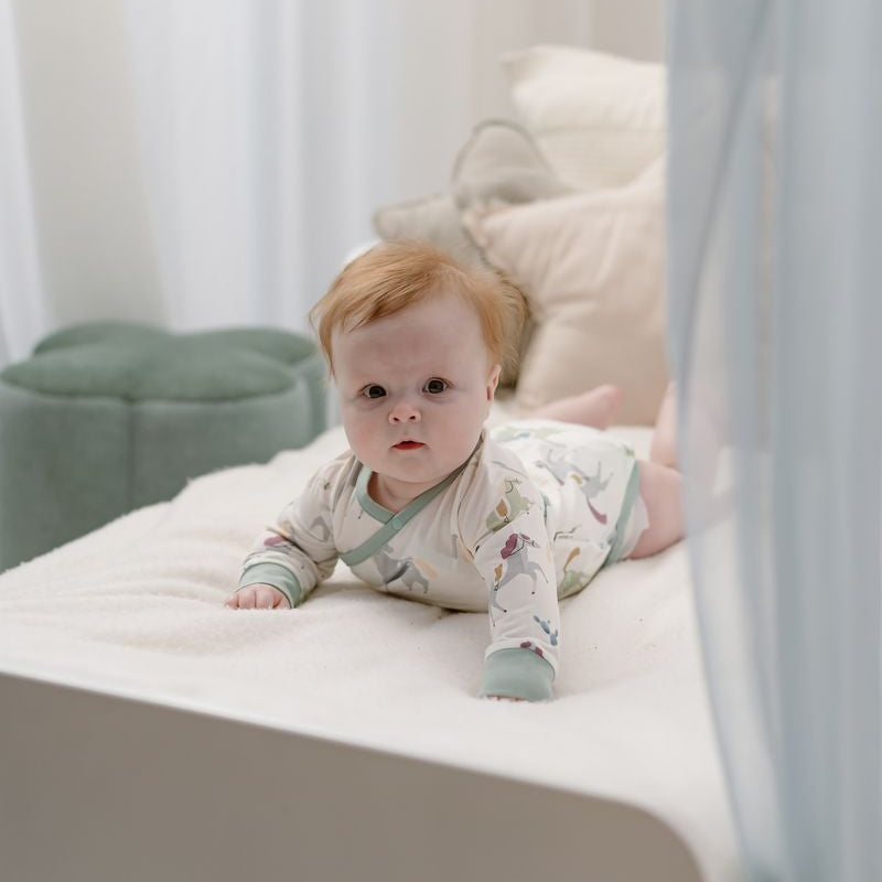 Nest Designs Pony Express Organic Cotton Long Sleeve Kimono Onesie in white with pastel print and mint cuffs, baby wearing