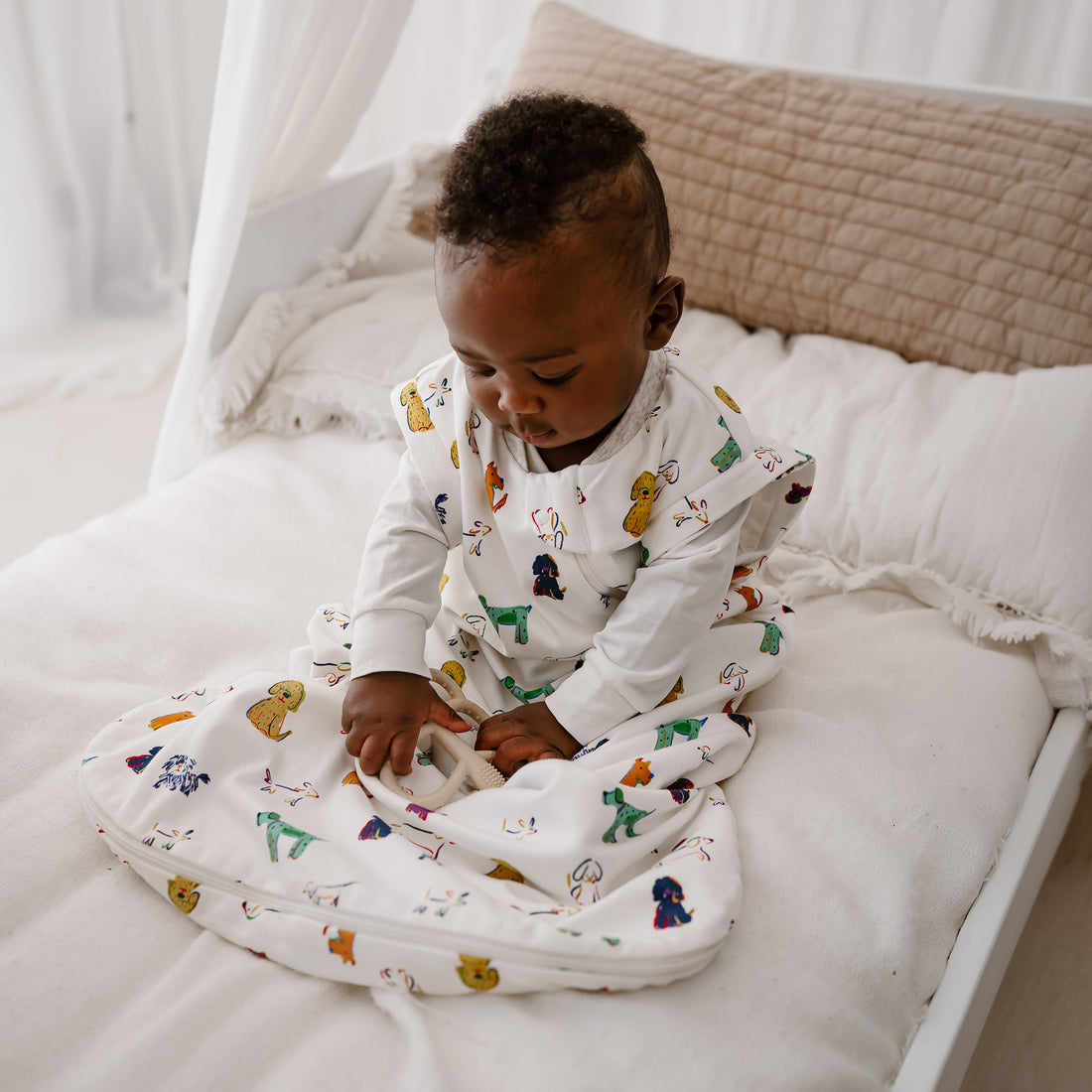 Toddler seated on a bed looking down while wearing the Bingo sleep bag