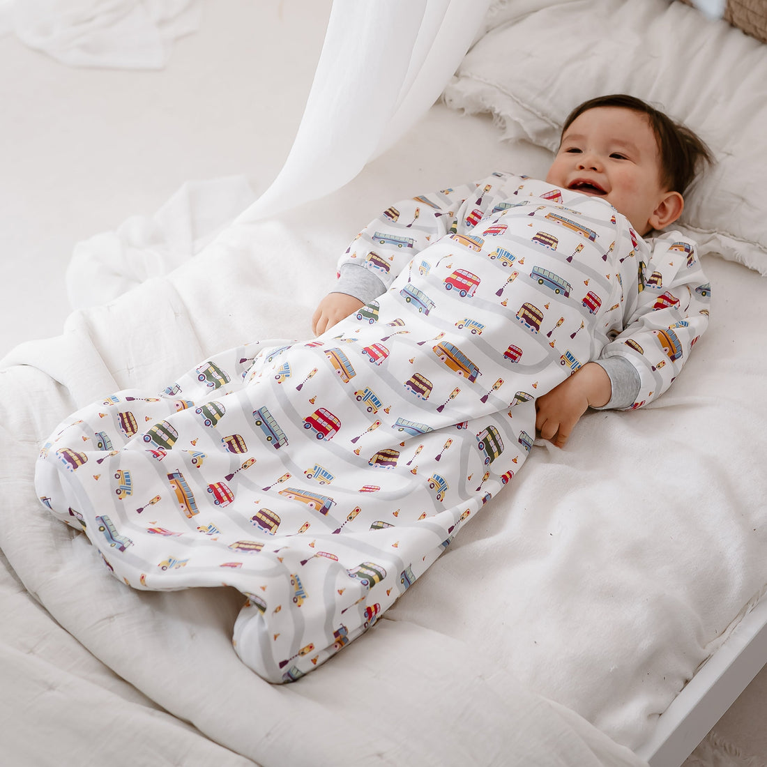 Smiling baby lying on a bed in the full-length Wheels On The Bus sleep bag