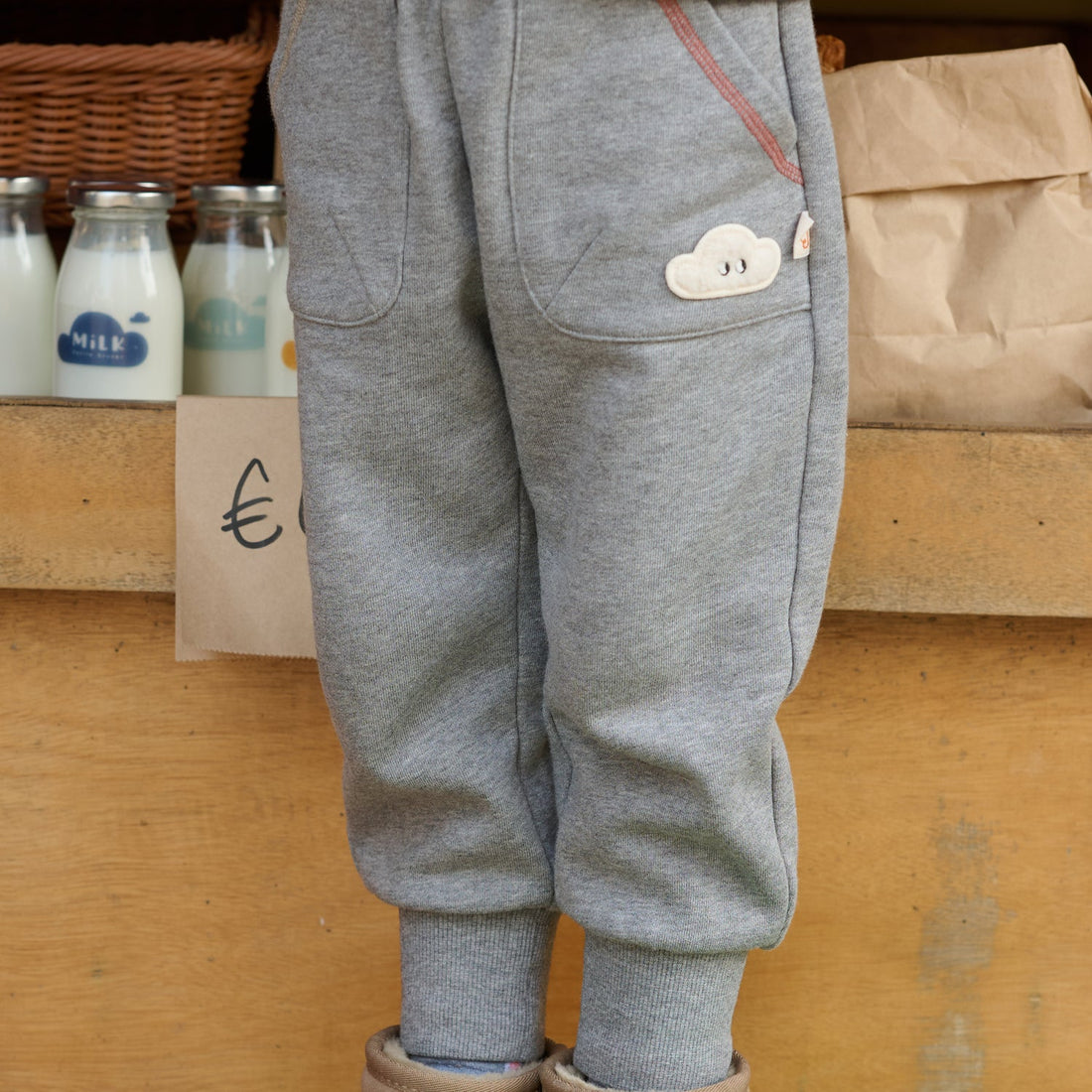 Nest Designs Joggers in Pebble Grey, worn close-up showing curved pockets, colored piping, cloud detail, and ankle cuffs