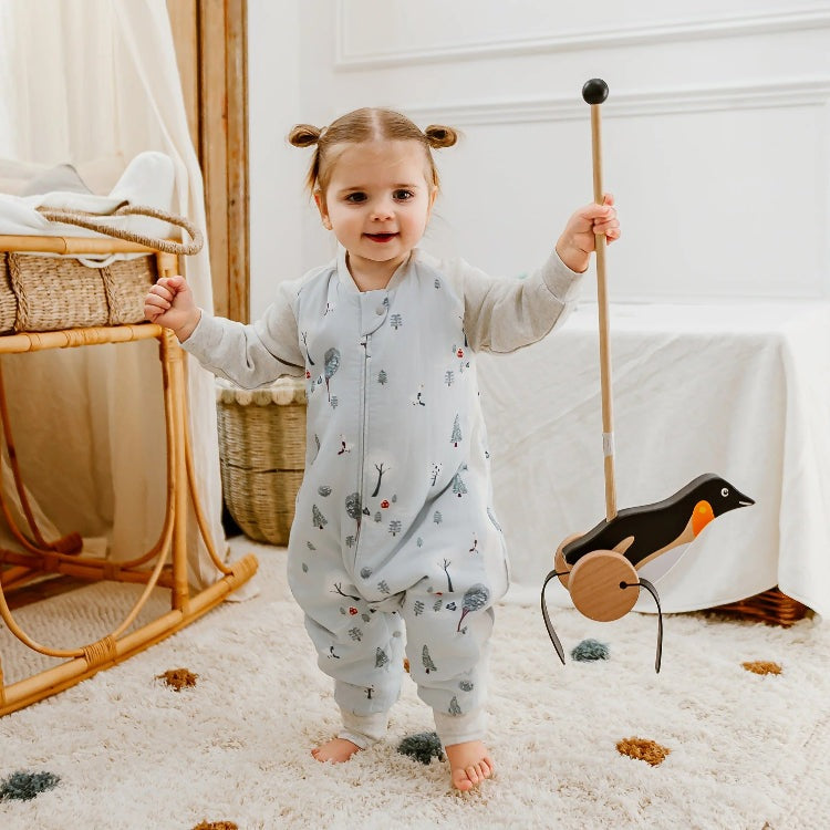 Nest Designs Raglan Bamboo Long Sleeve Footed Sleep Bag 2.5 Tog Snowy Snuggles, worn by a toddler walking indoors with a wooden pull-along toy.
