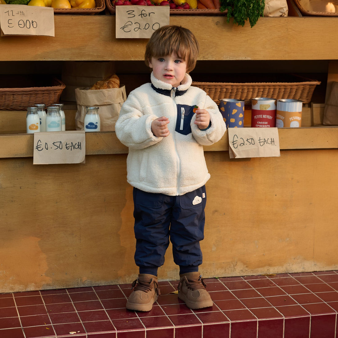 Nest Designs Nylon Pants in Blueberry navy, worn by a child holding a cup in front of a market counter