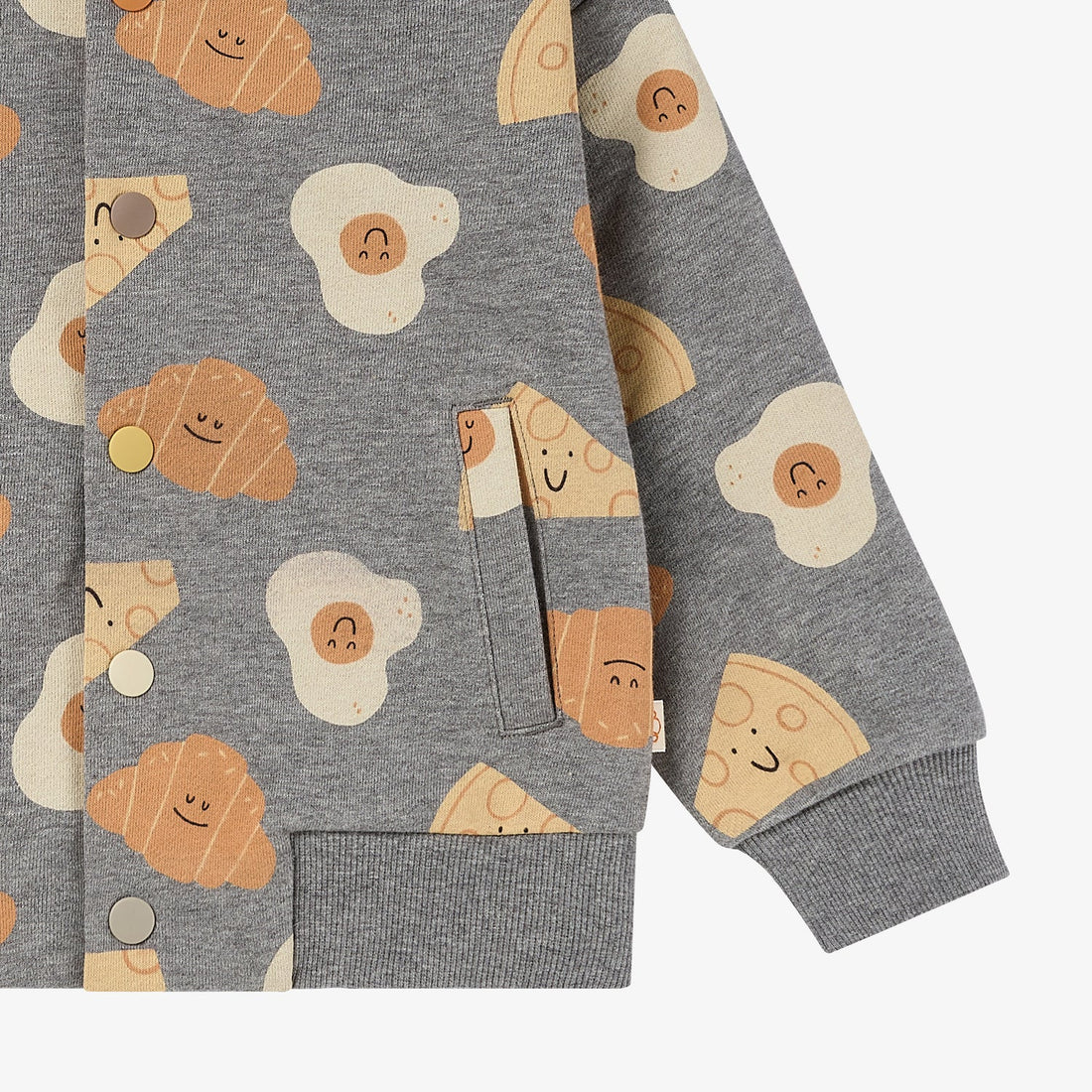 Nest Designs Smiley Side Up baseball jacket lower-front detail showing a welt pocket, grey ribbed hem and printed sleeve cuff