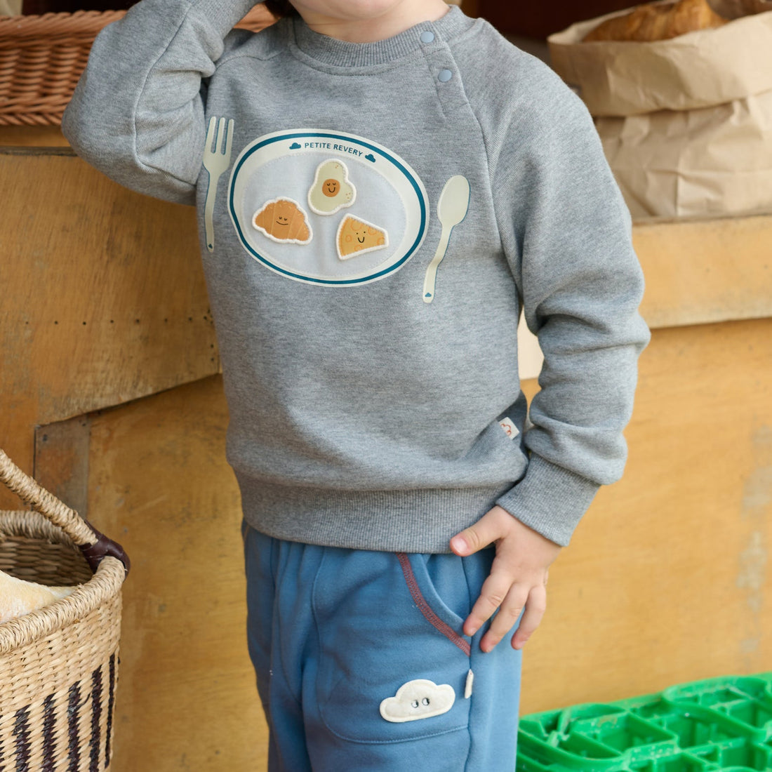 Nest Designs Smiley Plate Velcro Sweatshirt in Pebble Grey, worn close-up showing the shoulder snaps and plate graphic