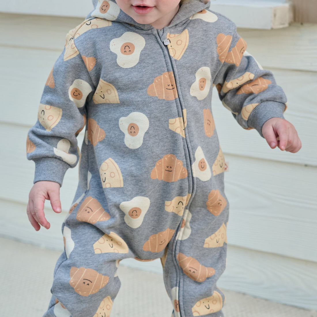 Nest Designs Smiley Side Up Hooded Romper in grey, front action view on a toddler walking with arms out