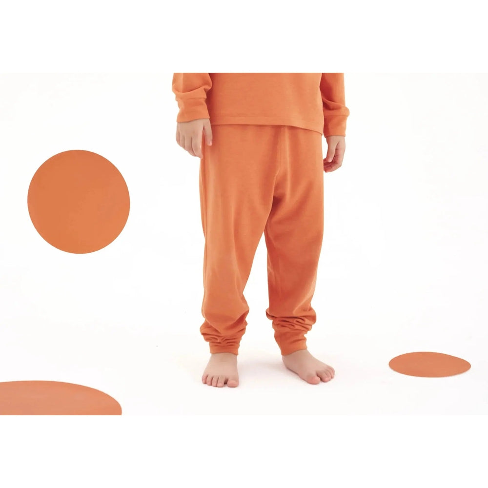 Nest Designs Tanboocel Pants Pantone Apricot Orange worn by a barefoot toddler, with cuffs gathered for a cozy fit.