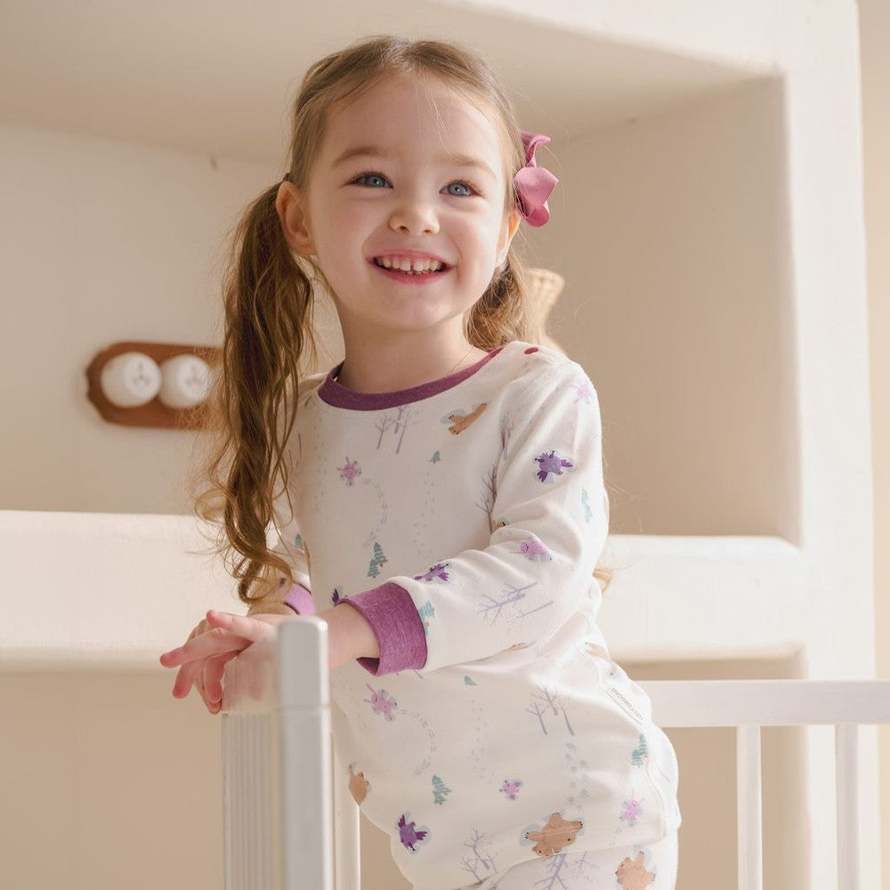 Nest Designs two-piece long-sleeve pajama set Snow Angels for toddlers; girl in white pajamas with pastel snowflakes.