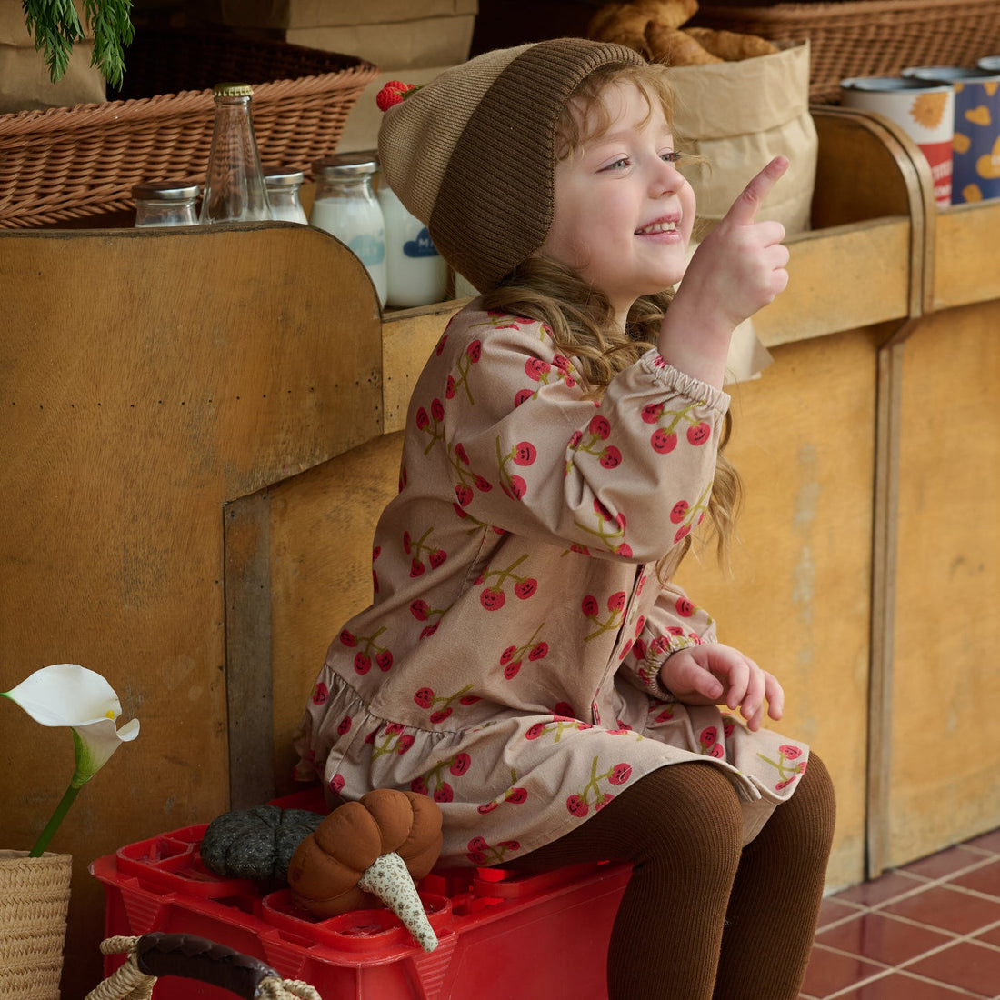 Nest Designs You're So Vine blush corduroy dress worn by a child pointing upward from a red market crate