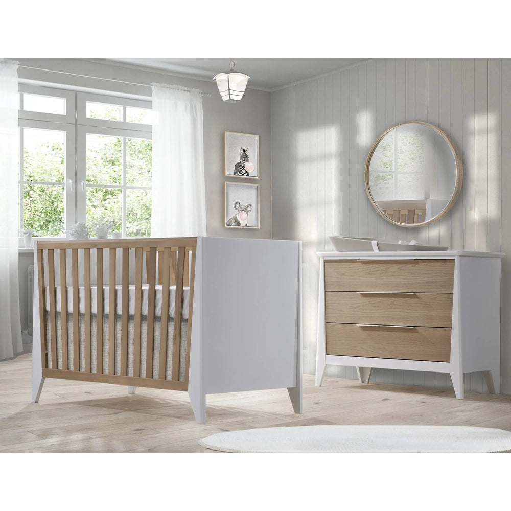 Nest Flexx Premium Classic crib in natural birch with white frame, beside a dresser with natural wood drawers in a bright nursery.