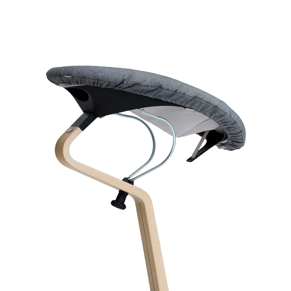 NOMI Baby high chair cushion in grey fabric attached to a light-wood frame with metal supports.