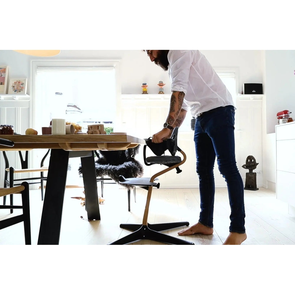 NOMI Chair White Oak high chair in light wood finish being assembled by a man in a bright kitchen.