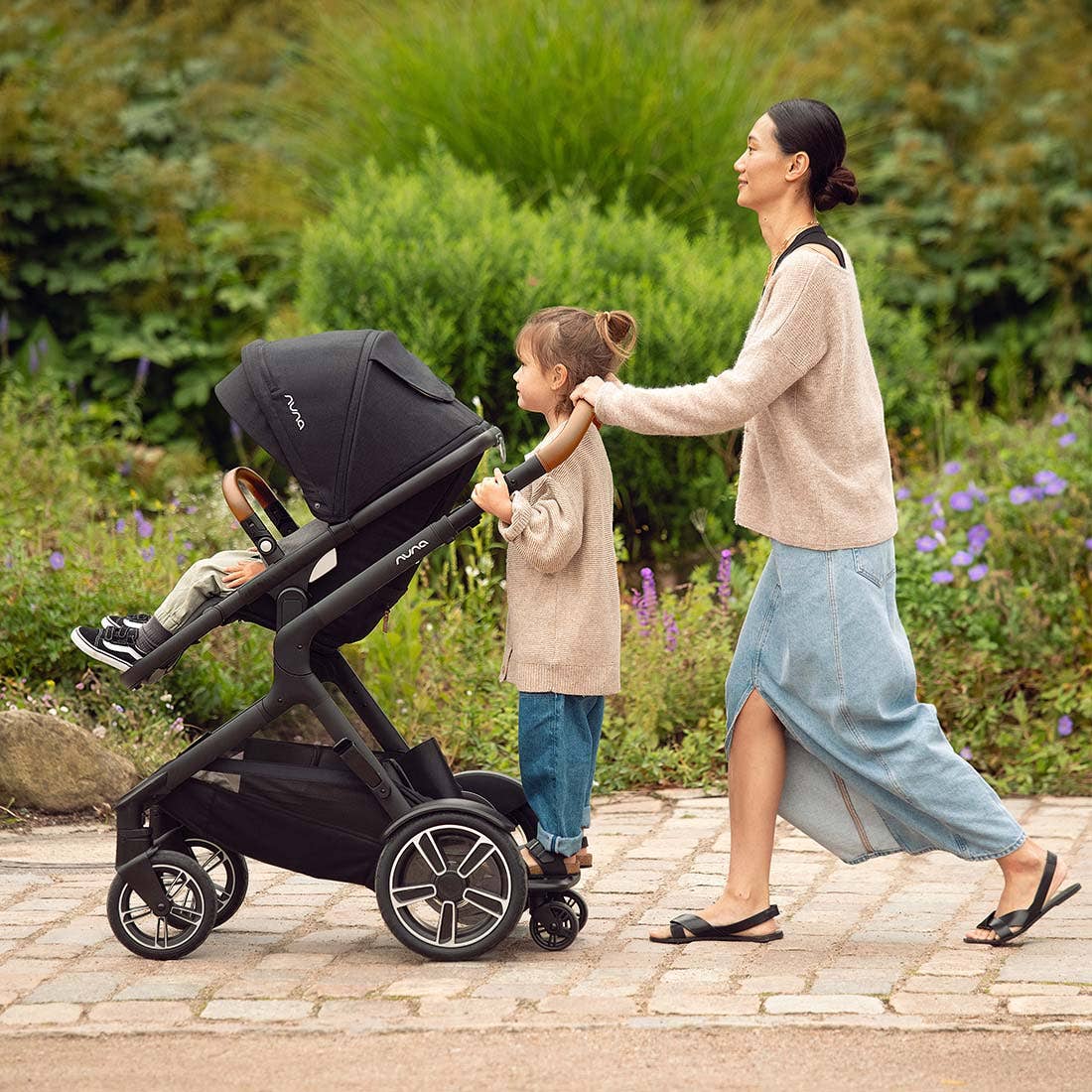 Nuna DEMI next Stroller with Rider Board — child riding on rear rider board during garden walk
