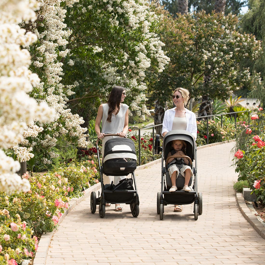 Nuna MIXX next Stroller — two adults pushing strollers along a garden path