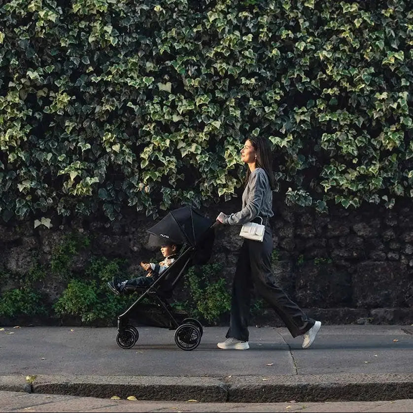 Nuna TRVL LX Stroller + PIPA Urbn Infant Car Seat Travel System showing Nuna TRVL lx Stroller — stroller walk beside ivy-covered wall