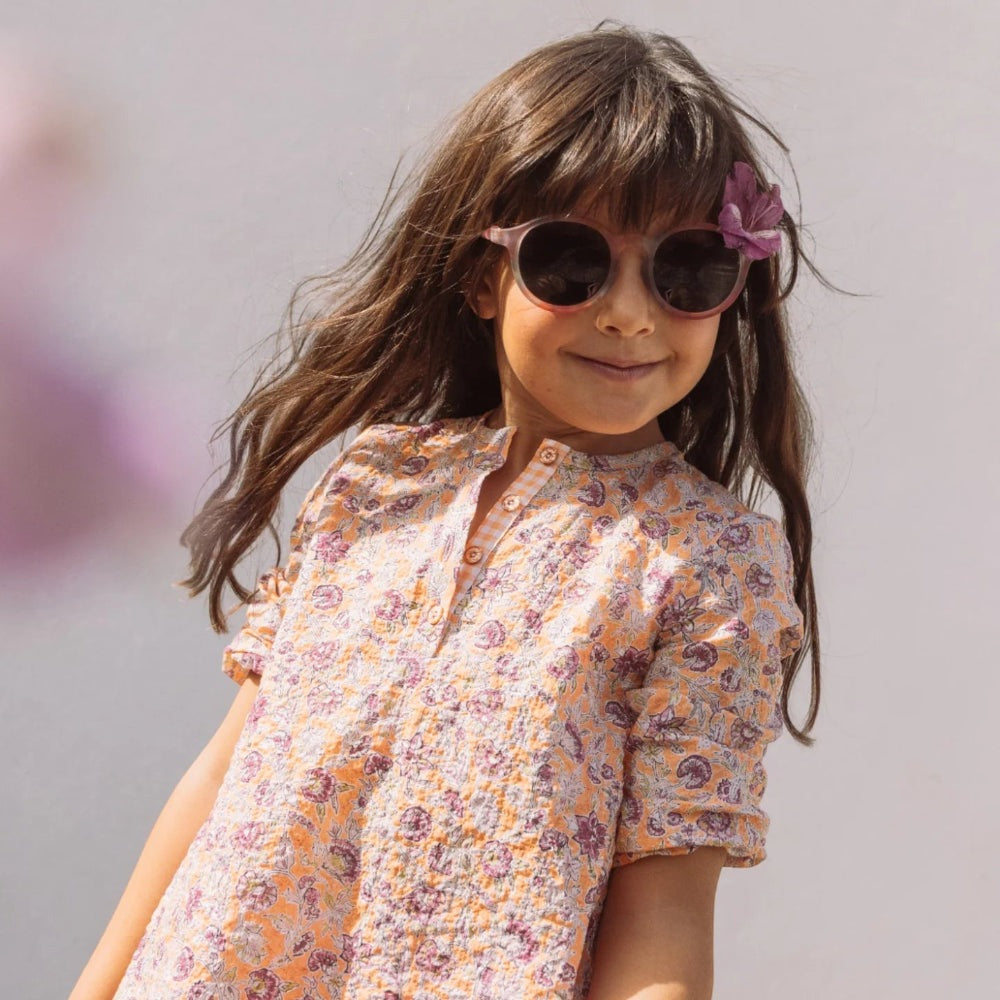 Olivio & Co Junior Oval Sunglasses in Rock Rose with pink lenses, worn by girl in floral dress