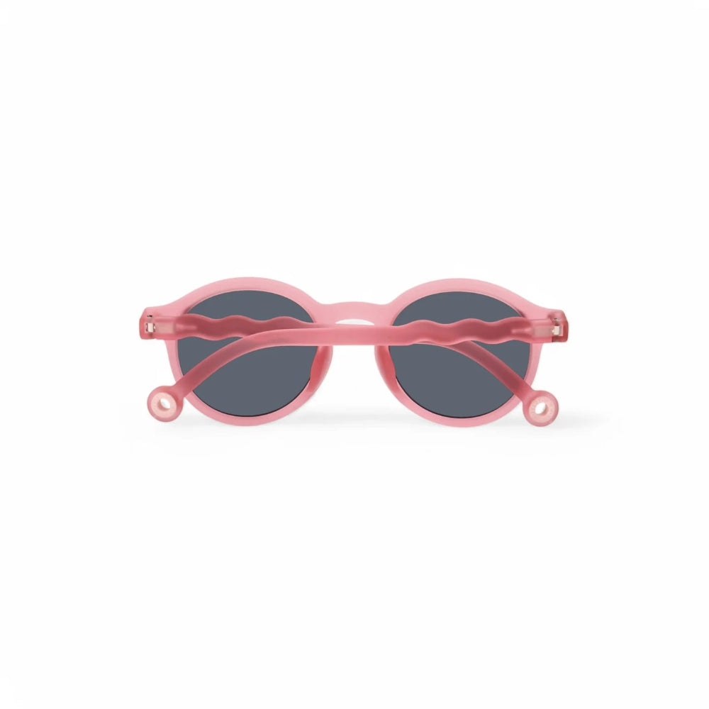 Olivio & Co junior oval sunglasses in rock rose pink with dark lenses and wavy arms.