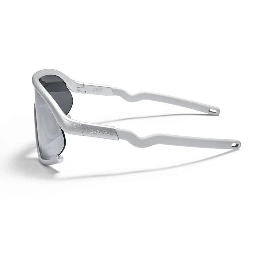 Olivio & Co Sport Sunglasses Kids/Junior Full-Rim Space Silver with grey lenses, temples extended on desk.