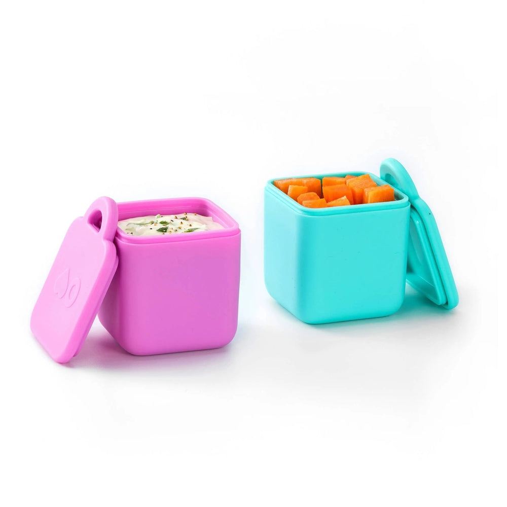 Omielife Omiedip Sets silicone lunch boxes in pink and teal, lids off as dip and carrot sticks are shown.