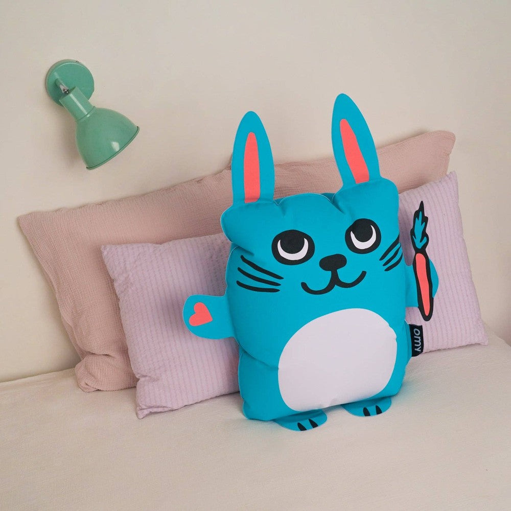 OMY Bunny Super inflatable pillow in bright blue with pink ears, resting on a sofa.
