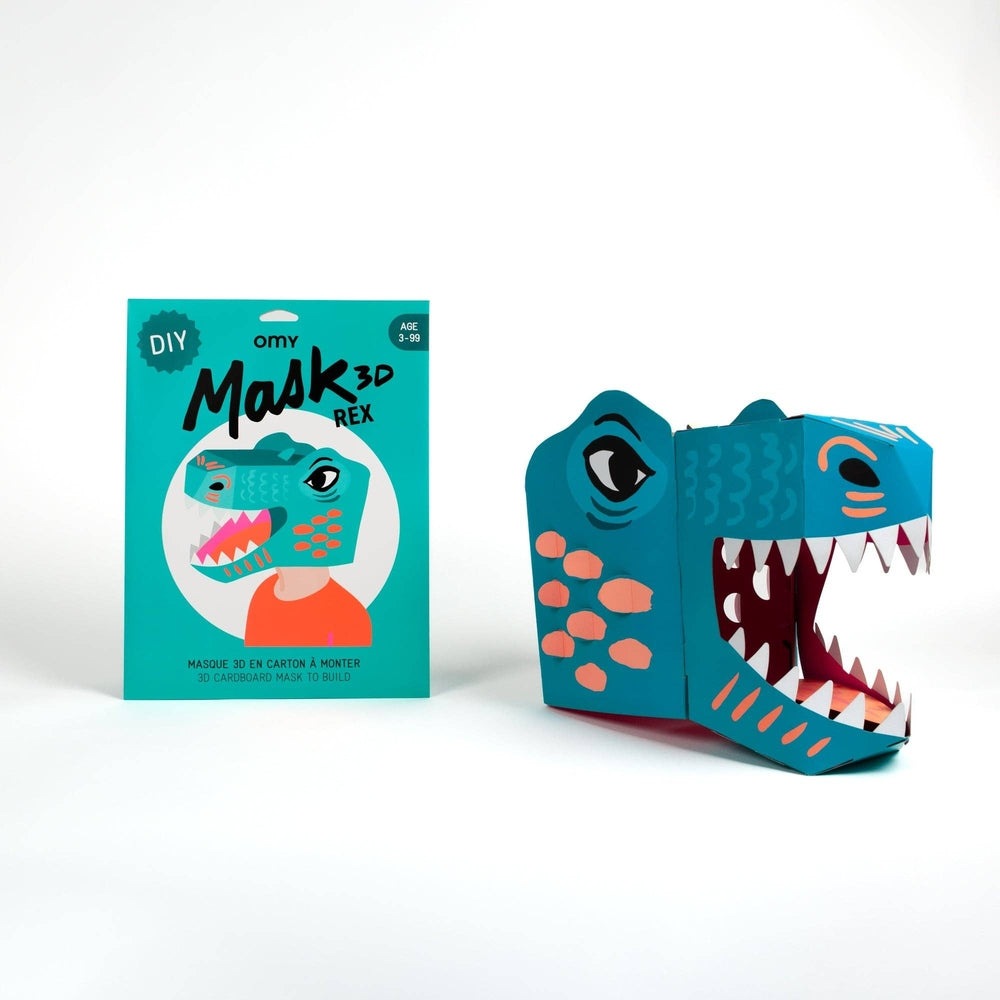 OMY Dino 3D mask: turquoise dinosaur mask with orange spots and open jaws, shown with its teal packaging.