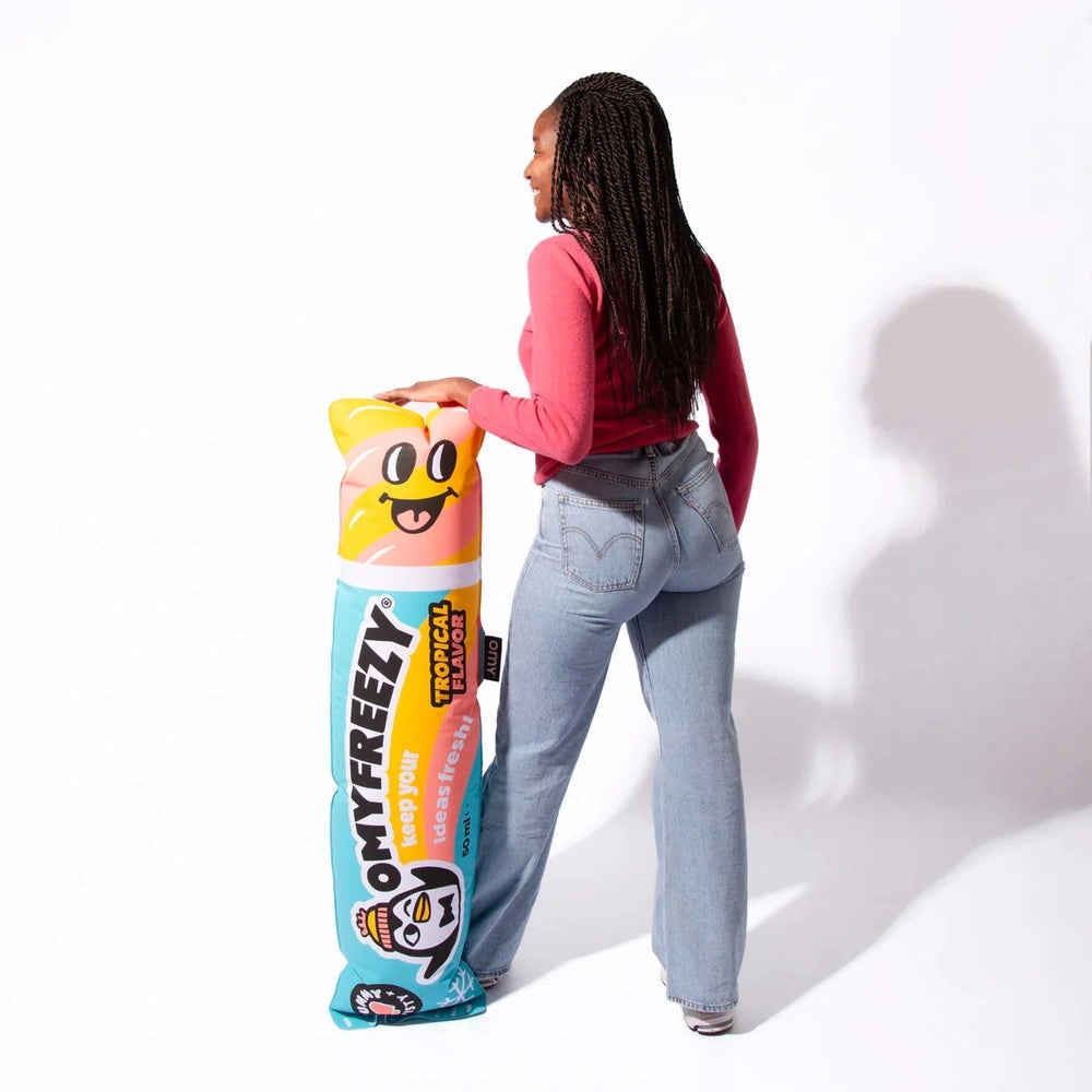OMY Freezy Giant inflatable pillow held by a woman in a pink sweater and jeans, featuring a colorful emoji design.