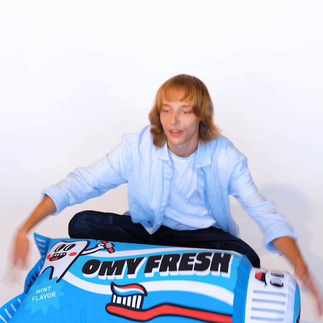 OMY Fresh Giant inflatable pillow, blue with mint flavor graphic, as a person sits on it for playful relaxation.