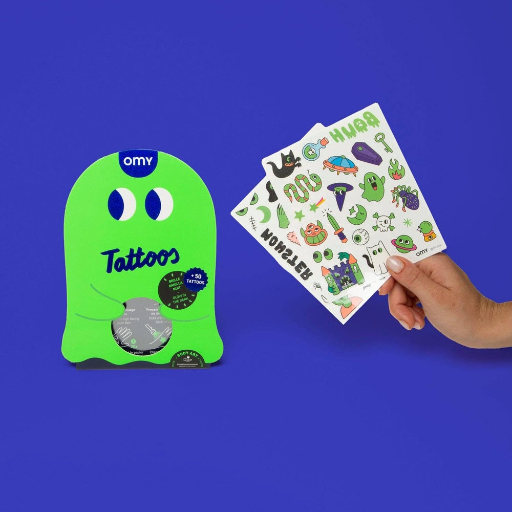 OMY Glow in the Dark Tattoos: neon green ghost package beside a hand holding colorful temporary tattoo sheets.