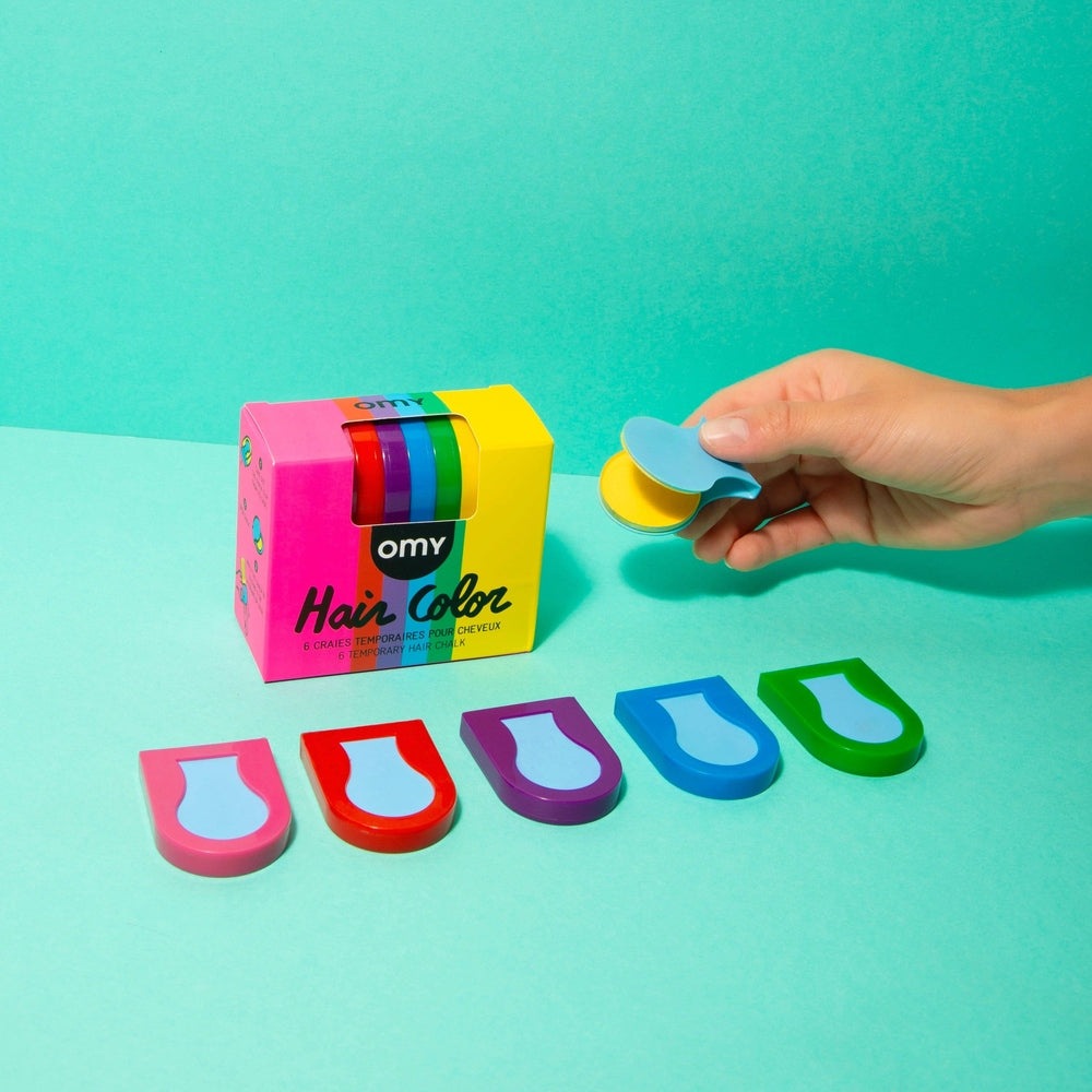 OMY Hair Chalk set with rainbow sticks and bright packaging, while a hand uses a blue/yellow applicator to apply color.