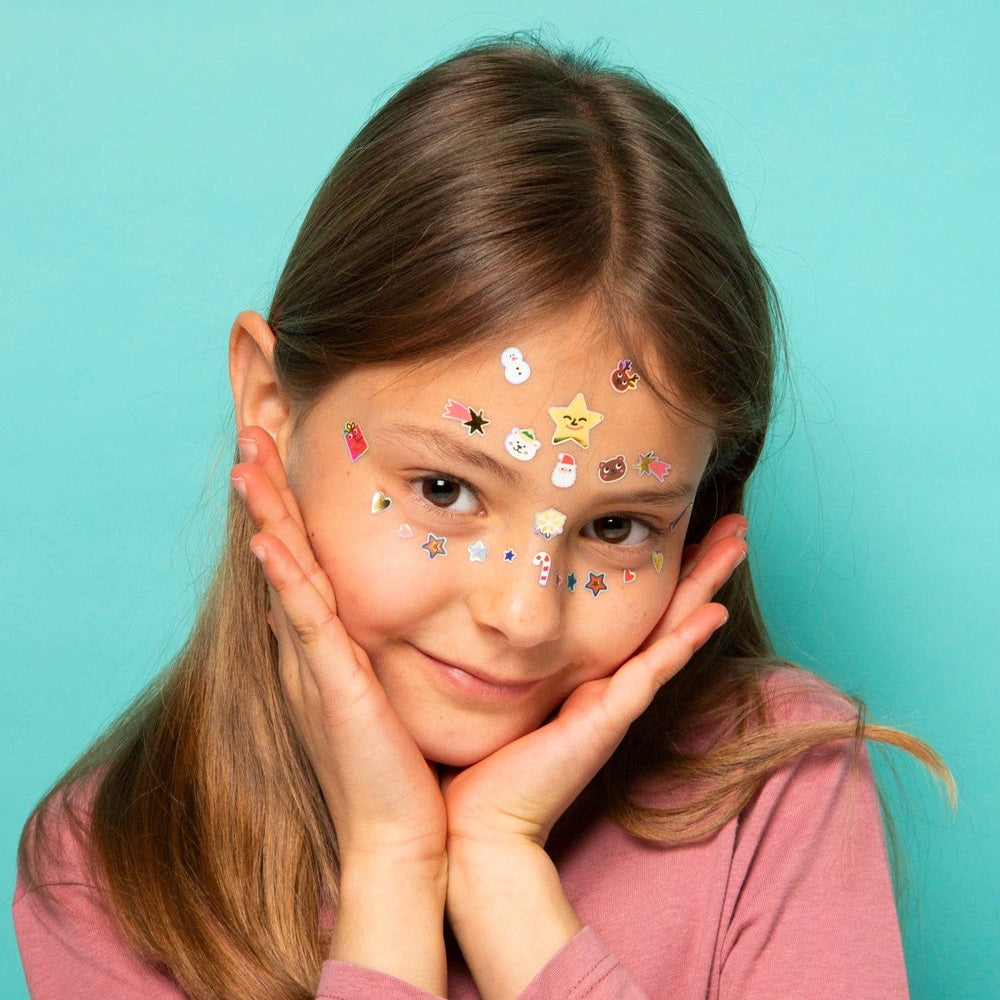 OMY Hohoho Holiday! Face stickers worn by a smiling girl with festive stickers on forehead and cheeks.