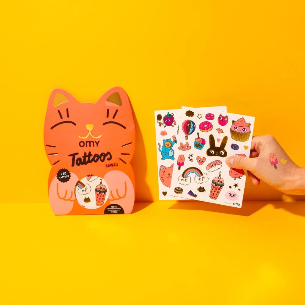 OMY Tattoos Kawaii cat-shaped package beside a colorful sticker sheet, hand showing a tiny kawaii temporary tattoo on finger.