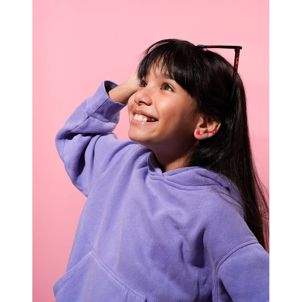 OMY - Kids sticker earrings Unicorn worn by a smiling girl in a lavender hoodie, showcasing colorful unicorn earrings on her ears.