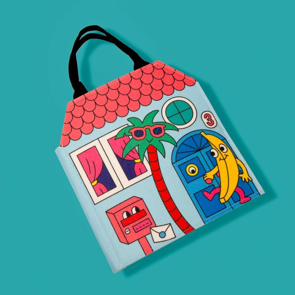 OMY Montessori Play Kit tote in light blue with playful house scene and palm tree; black carry handles.