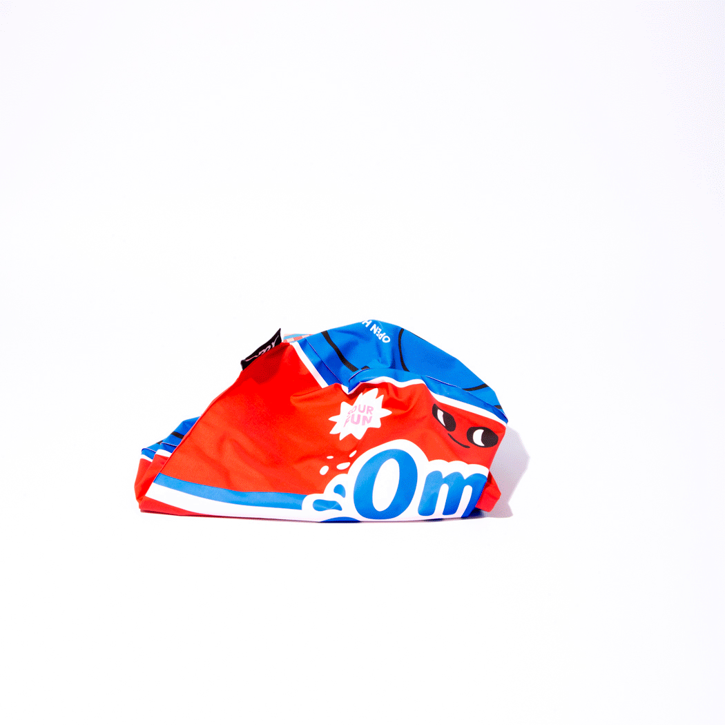 OMY Cola Giant inflatable pillow, vibrant red/blue graphics, folded on white background.