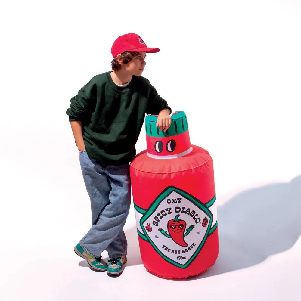 OMY Spicy Diablo giant inflatable pillow held beside a person, bright red with green cap.