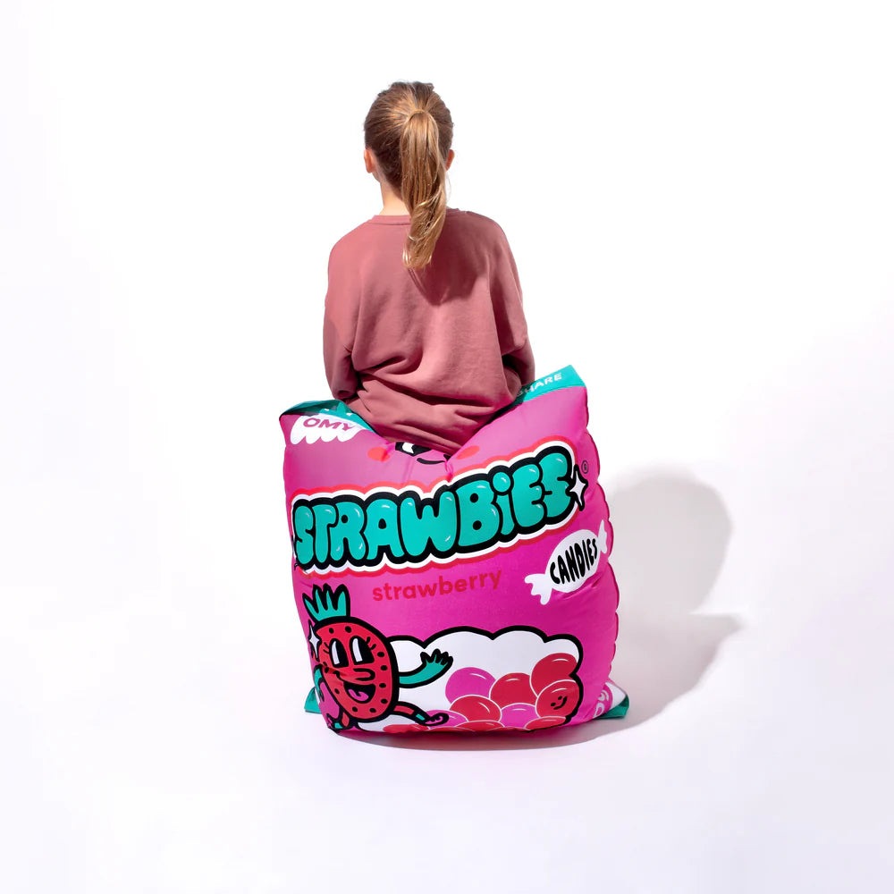 OMY Strawbies Giant inflatable pillow in pink, featuring strawberry graphic as a person sits on it.