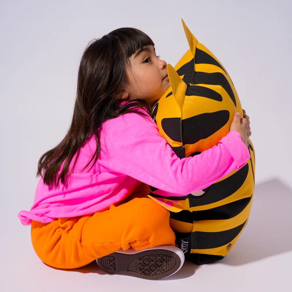 OMY - Tiga - Super inflatable pillow held by a smiling child in a pink shirt and orange pants.