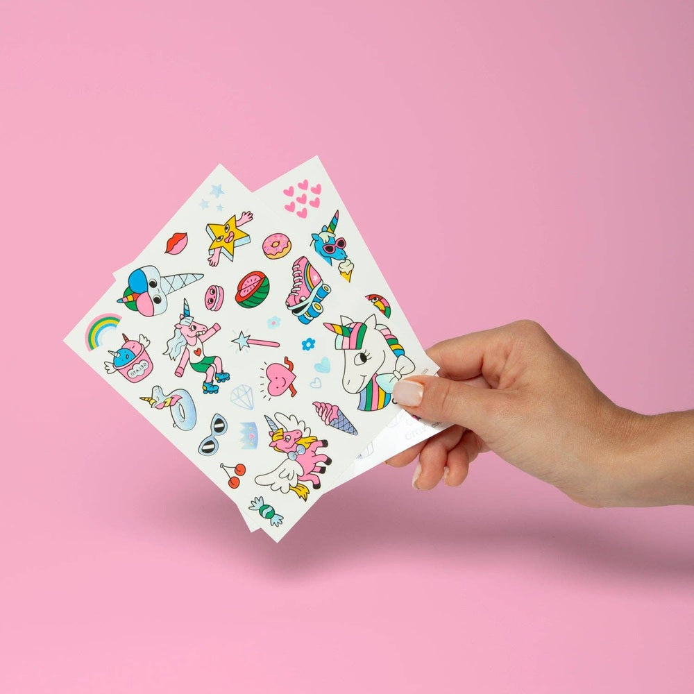 OMY - Unicorn - Tattoos sheet held by hand against pink backdrop, colorful unicorns and sparkles for temporary body art