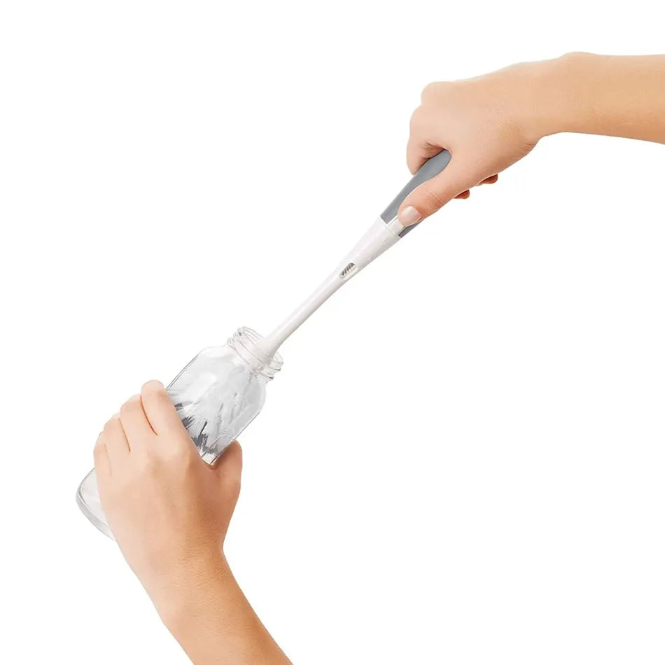 OXO Tot soap-dispensing bottle brush with gray handle cleaning a baby bottle