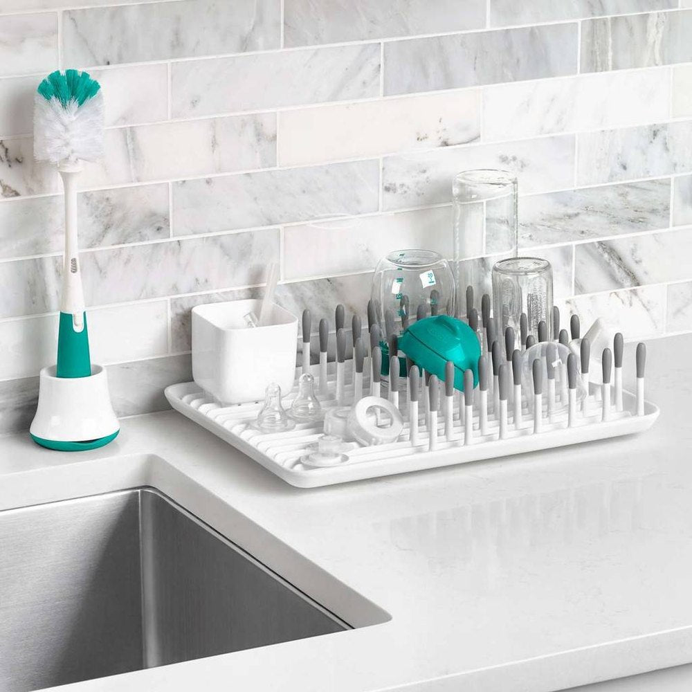 OXO Tot soap-dispensing bottle brush with stand in teal and white on a kitchen dish rack