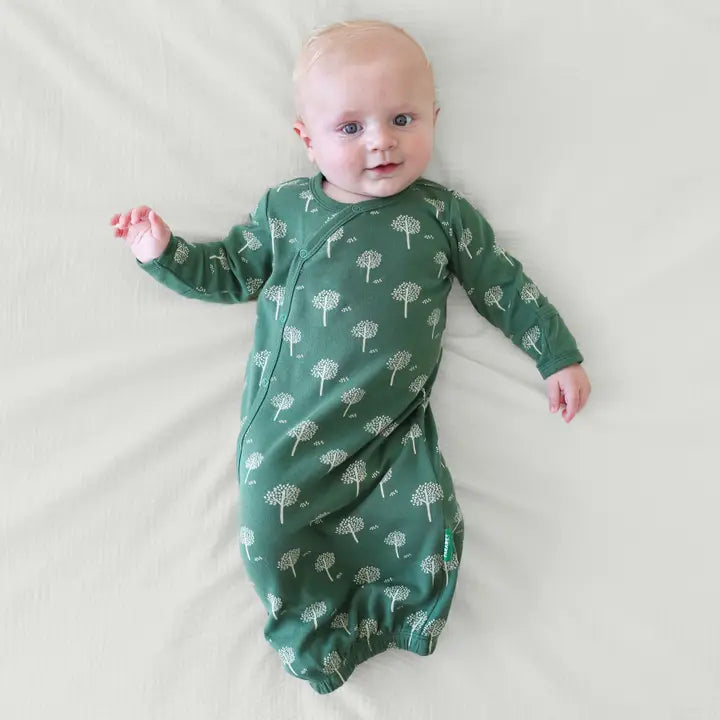 Parade Organic Gowns Signature Prints baby one-piece in green with white tree motif, baby relaxing on white sheets.