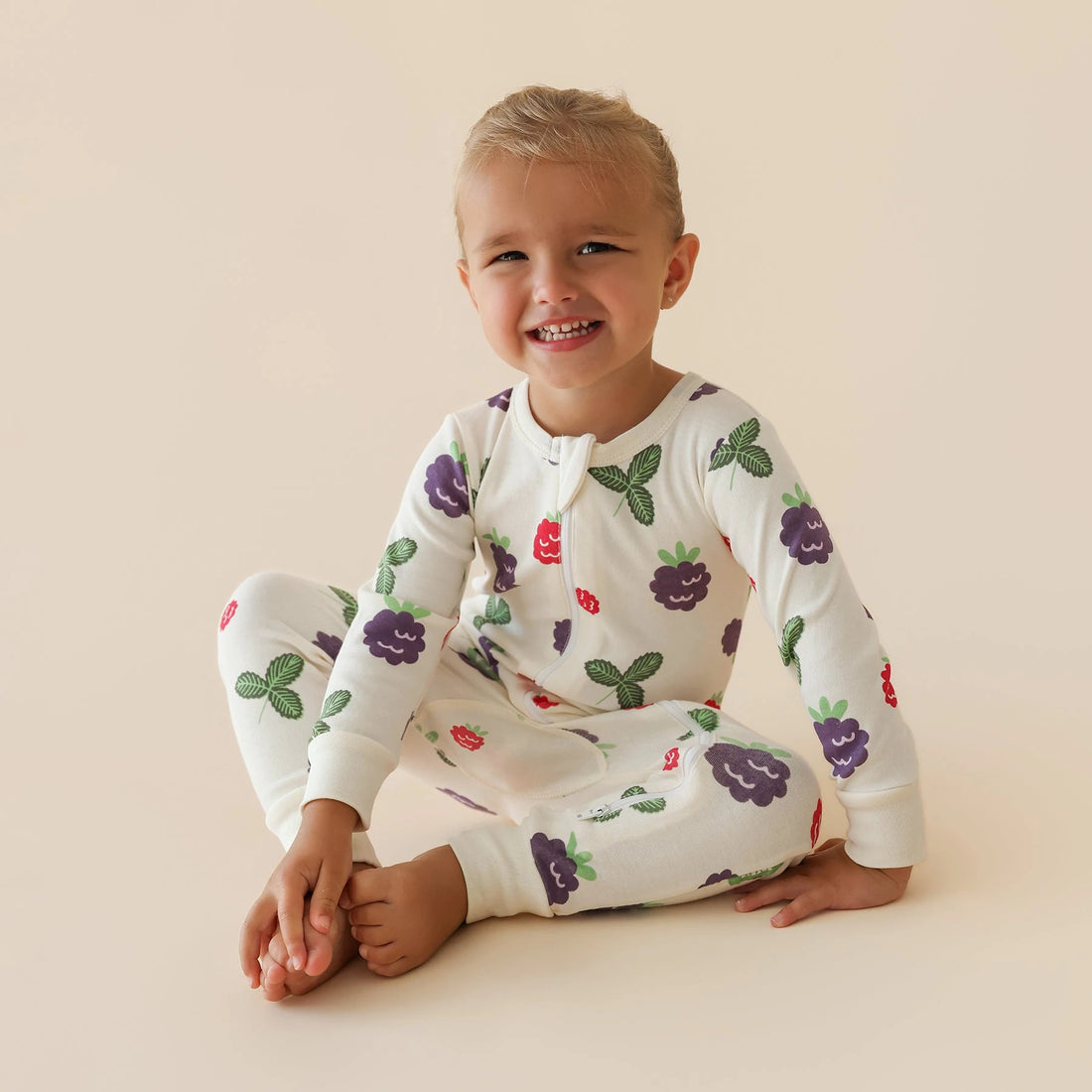 Child wearing a Parade Blackberries organic two-way zip romper while sitting.