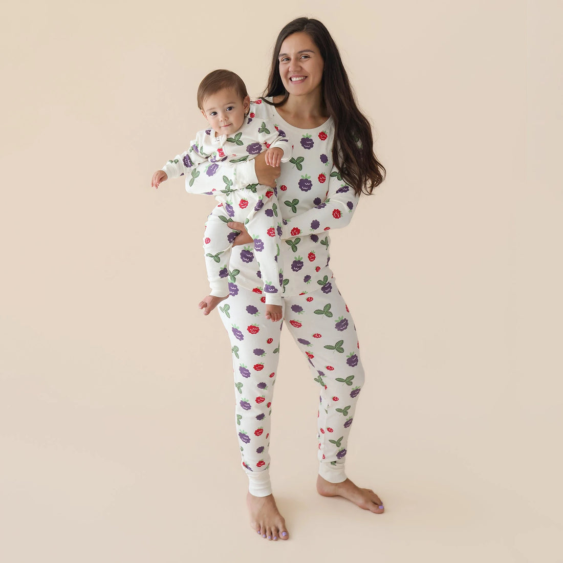 Parent holding a baby wearing a Parade Blackberries organic two-way zip romper.