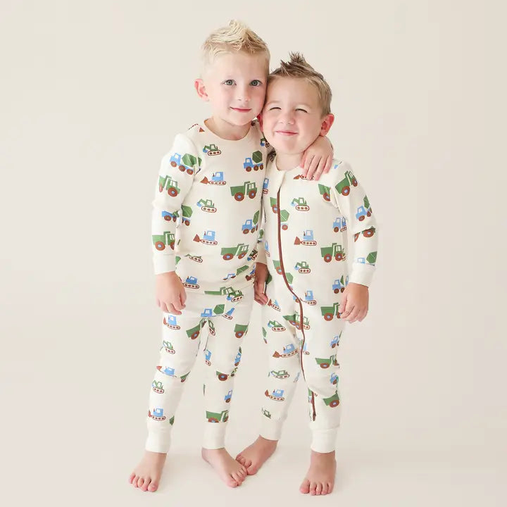 Parade Organic Signature Print 2-Way Zip Romper; two toddlers in cream tractor-print rompers, arms around each other.