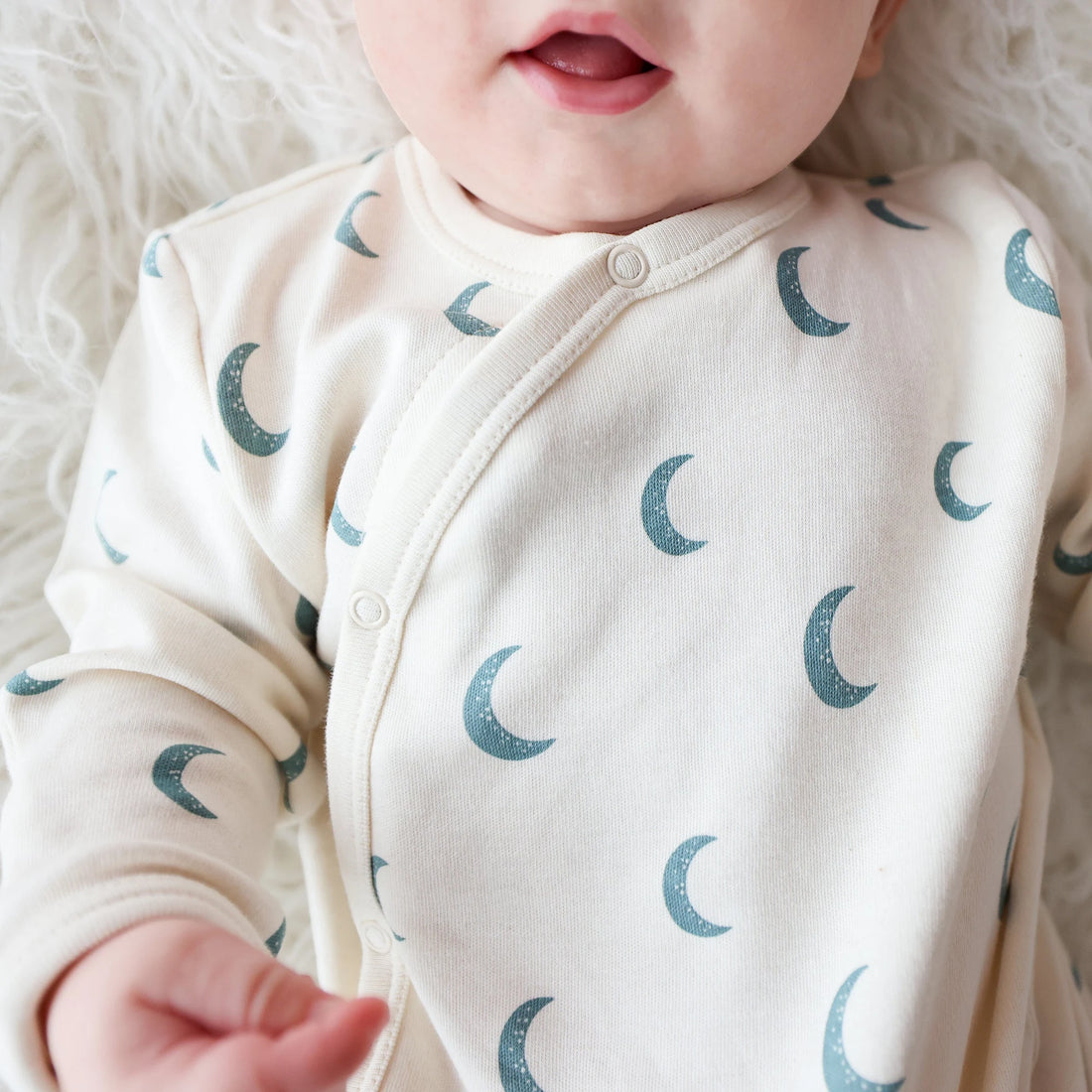 Baby wearing a Parade Blue Moons organic wrap gown, showing the snap-front neckline and crescent print.