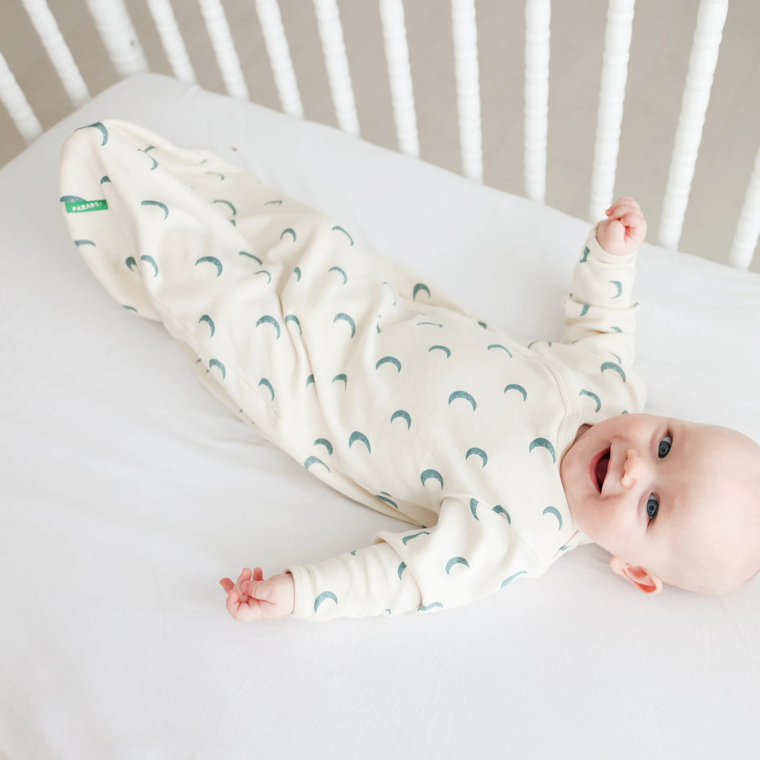 Baby wearing a Parade Blue Moons organic gown on white bedding.