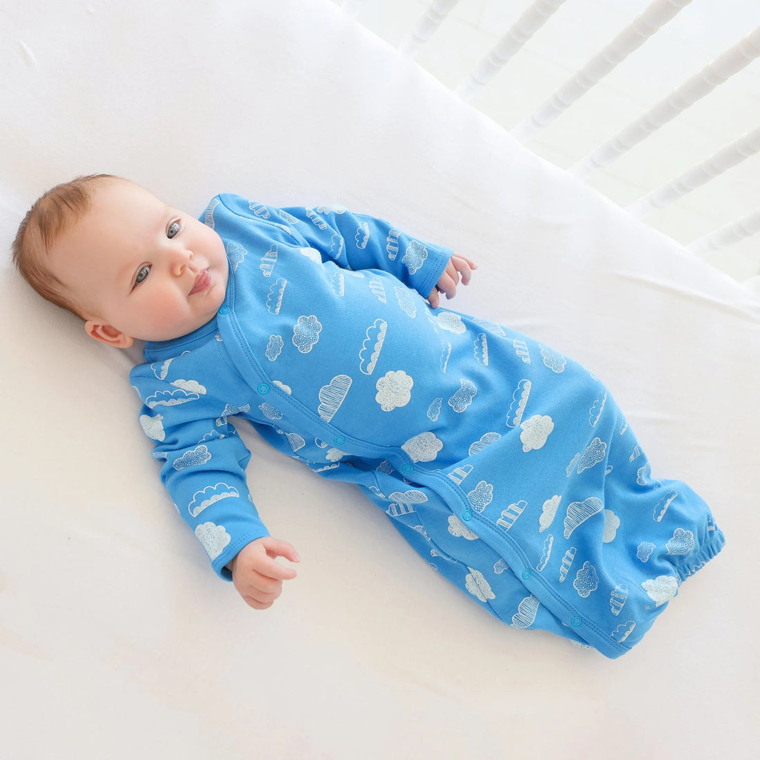 Baby wearing a Parade White Clouds organic gown on white bedding.