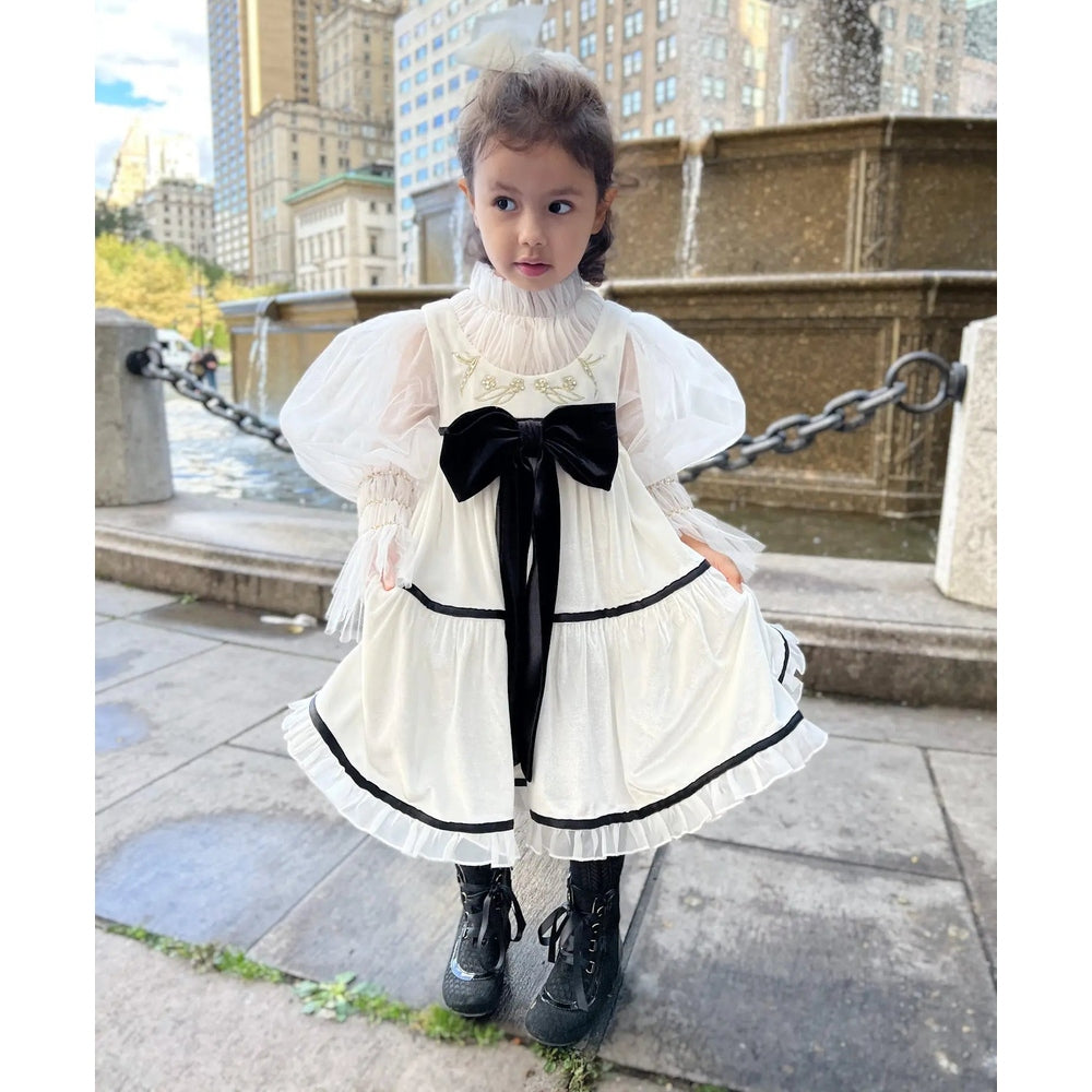 Petit Maison Kids Aurora Ivory Velour Dress with sheer puff sleeves and a black bow, girl twirls to show the tiered hem.